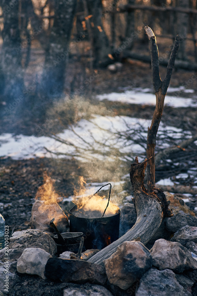 cooking at campfire in the forest . Black charred pot at bonfire with clouds of smoke in sunset lights. Trekking or hiking cuisine in the wild nature. cooking at campfire in the forest . Black charred pot at bonfire with clouds of smoke in sunset lights. Trekking or hiking cuisine in the wild nature.
