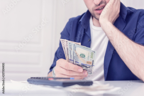 Male calculates his monthly expenses, man does not have enough money for all his debts, bills and calculator on the table, cropped image, closeup, toned