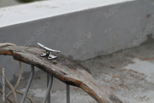 A stainless steel bollard with rainwater dripping on it, bolted with rusty screws to an old plank on the side of the boat. Summer day, Beloe lake. photo