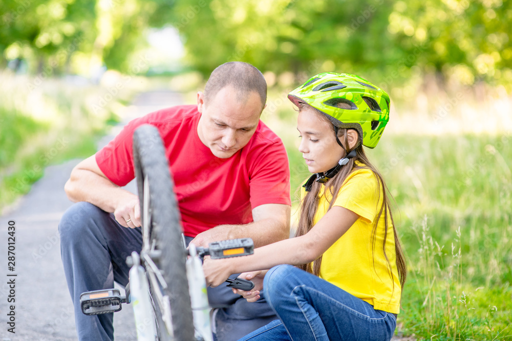 Happy family. Father helps daughter to pump bicycle wheel in summer park