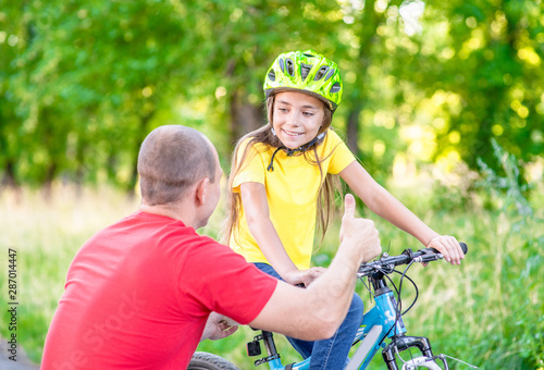 Father talking with his  daughter, teaching her how to ride a bicycle and showing thumbs up