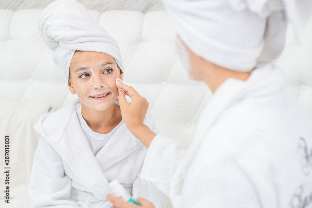 Mom cleans her daughter's face with a cotton pad and lotion Mom cleans her daughter's face with a cotton pad and lotion