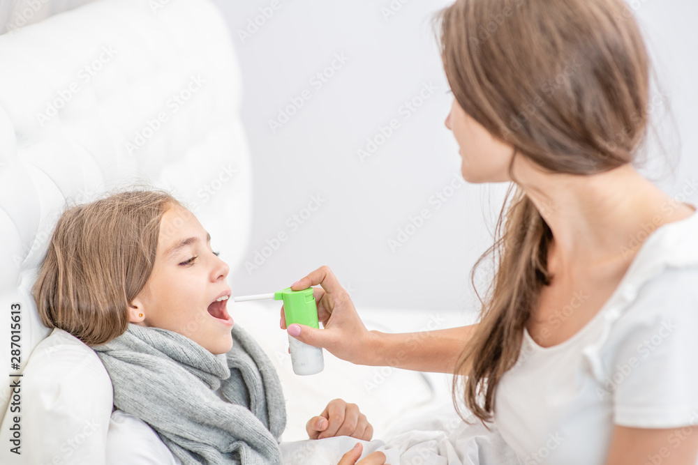 Woman using medical spray for young girl at home Woman using medical spray for young girl at home