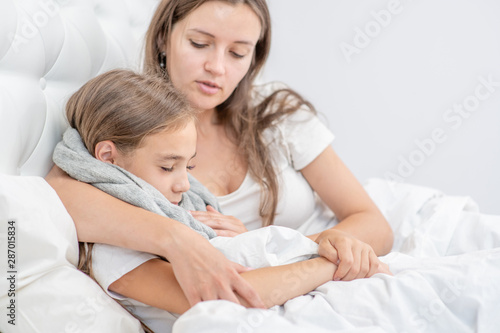 Young mom embracing her sick little girl on the bed at home