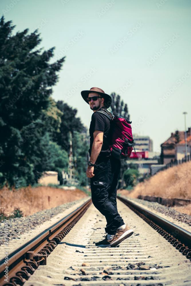 A man with a backpack goes ahead on the railway track during the summer season. Long way concept, forward. achieve your goal, the beginning of the path. cowboy hat and glasses, vertical photo A man with a backpack goes ahead on the railway track during the summer season. Long way concept, forward. achieve your goal, the beginning of the path. cowboy hat and glasses, vertical photo
