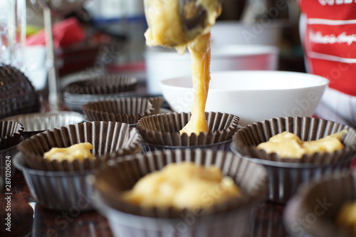A detailed close-up of a hand carefully spooning a portion of golden banana cupcake batter into a paper liner, illustrating a key step in the baking process.