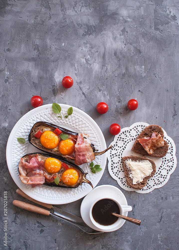 Baked eggplant stuffed with eggs and bacon on a plate, a Cup of coffee, fried toast on a gray concrete background. Breakfast idea. The view from the top. Copy space