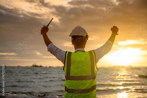 Success Engineer standing back during sunrise overlay with sea. The concept of engineering construction