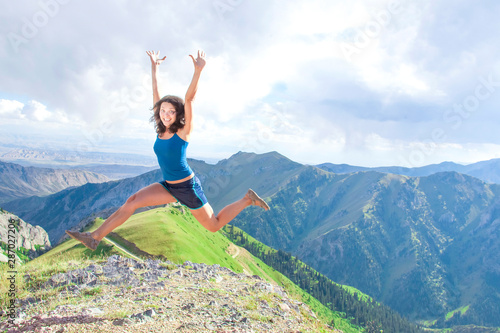 Positive girl with arms raised in a jump against a background of mountains.