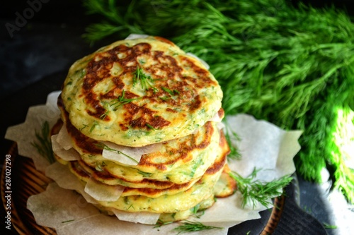 Appetizing pancakes on a wooden board. A photo of food in low key. Pancakes with parsley and chives. Ukrainian and Russian cuisine. Food on a black background. Pancake week.