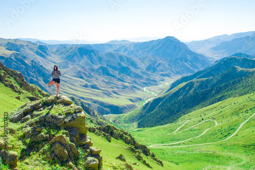 A girl in a yoga pose is standing on top of one of the mountains..