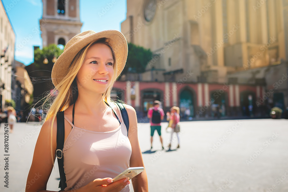 Europe travel summer tourism holiday vacation background - young attractive Caucasian smiling beautiful blonde girl face with hat mobile cell phone and using backpack in hand having chat in city