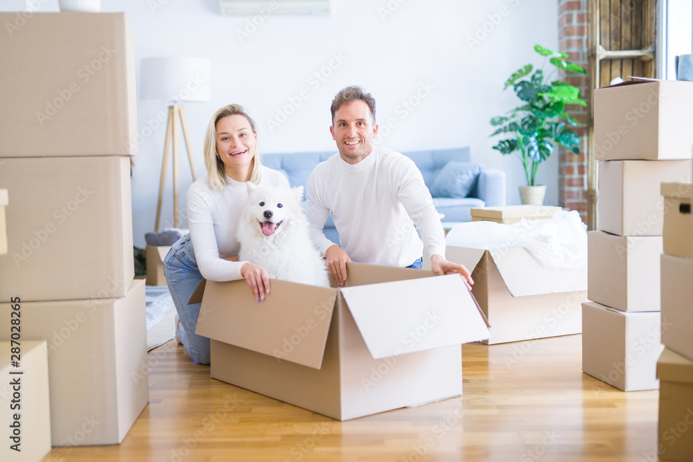 Fototapeta premium Young beautiful couple with dog sitting on the floor at new home around cardboard boxes