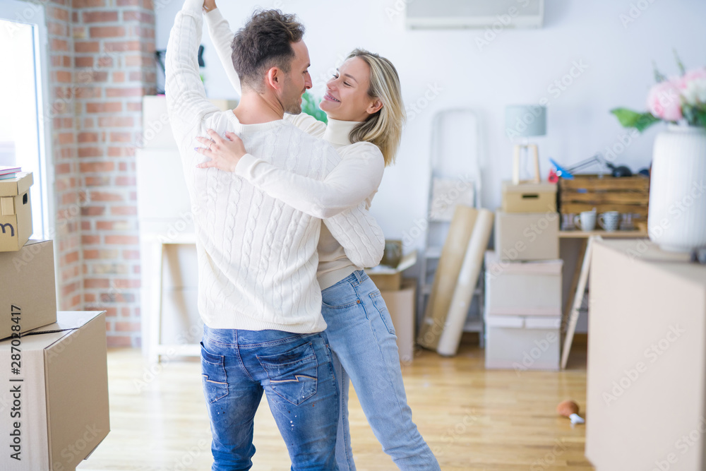 Obraz premium Young beautiful couple dancing at new home around cardboard boxes