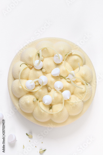 Contemporary Jasmine Tea, Cherry and Lychee Mousse Cake, covered with velvet spray coating, decorated with meringue cookies, dried jasmine buds and white chocolate elements, on white background.