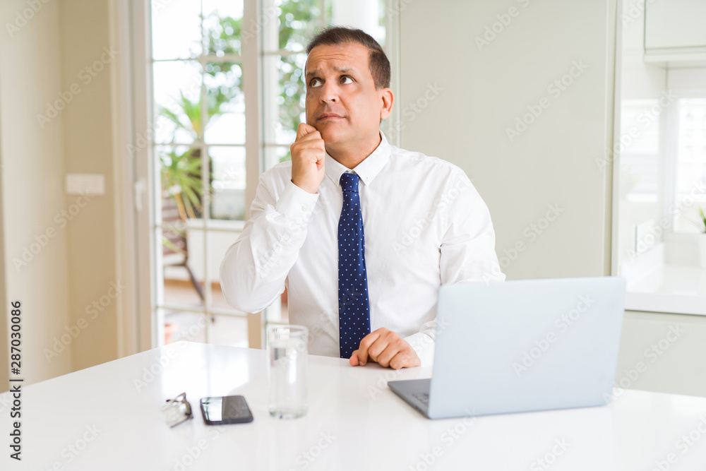Middle age business man working with computer laptop with hand on chin thinking about question, pensive expression. Smiling with thoughtful face. Doubt concept.