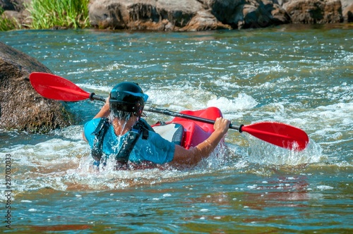 Playboating. A man sitting in a kayak with oars in his hands performs exercises on the water. Kayaking freestyle on whitewater. Eskimo roll. photo