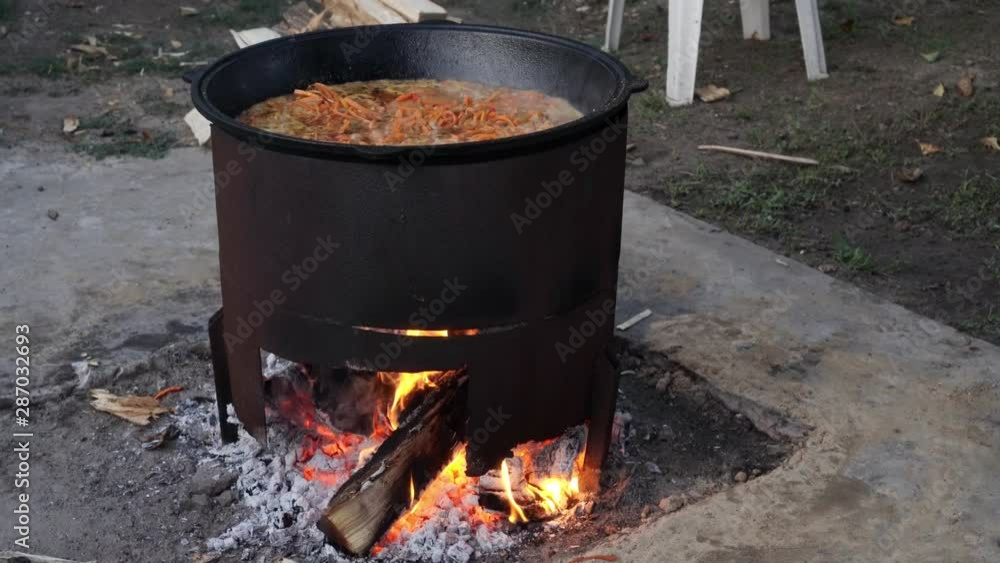Cooking pilaf in a large pot over an open fire. Fry meat, onions, carrots. Delicious rice. Street kitchen. Cooking pilaf in a large pot over an open fire. Fry meat, onions, carrots. Delicious rice. Street kitchen.