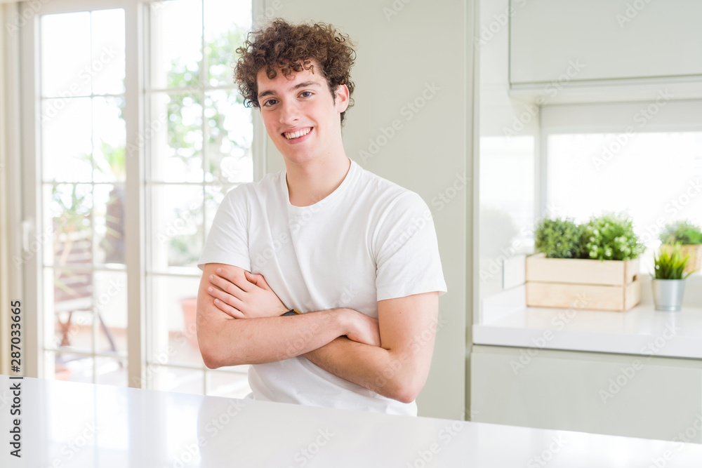 Young handsome man wearing white t-shirt at home happy face smiling with crossed arms looking at the camera. Positive person. Young handsome man wearing white t-shirt at home happy face smiling with crossed arms looking at the camera. Positive person.