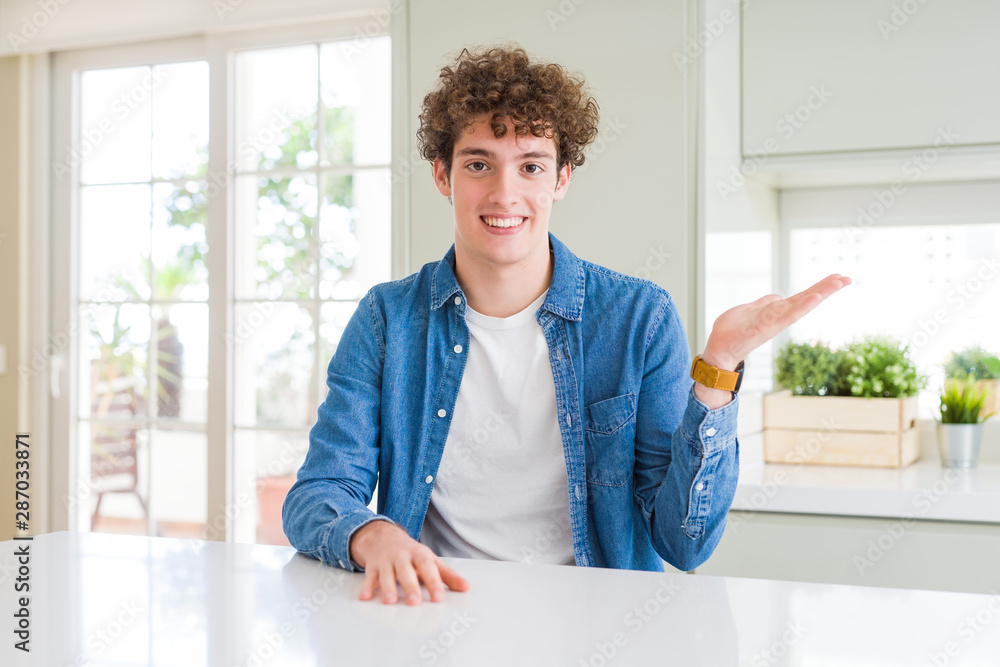 Young handsome man wearing casual denim jacket at home smiling cheerful presenting and pointing with palm of hand looking at the camera.