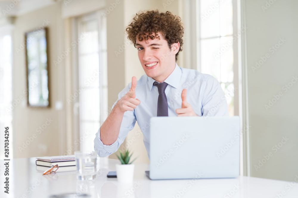 Young business man working with computer laptop at the office pointing fingers to camera with happy and funny face. Good energy and vibes.