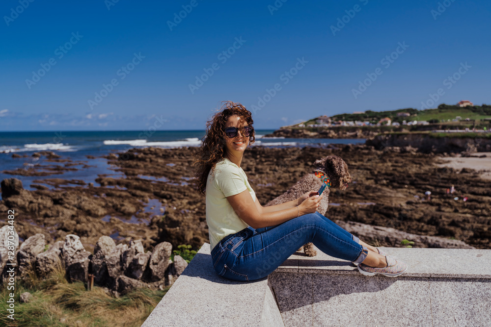 young woman and her cute spanish water dog outdoors enjoying together on a sunny and windy day. Summertime, love for animals and holidays concept