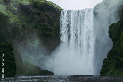 Fototapeta Naklejka Na Ścianę i Meble -  Majestic Skogarfoss waterfall in Iceland. White and green splashes flying all around against green hills covered with moss.