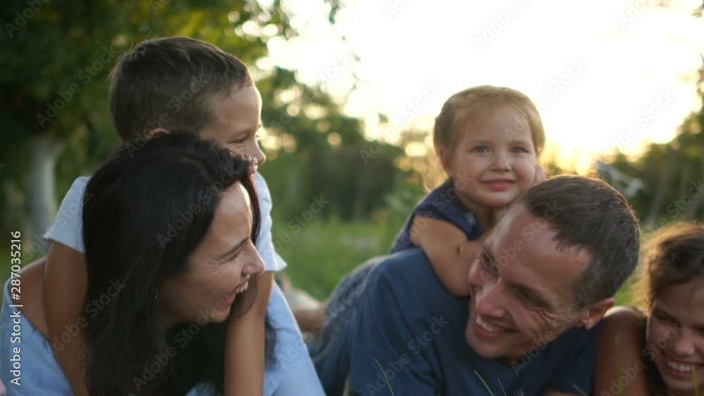 Happy young family with three children resting lying in the grass in the village. Summer holidays, family day Happy young family with three children resting lying in the grass in the village. Summer holidays, family day
