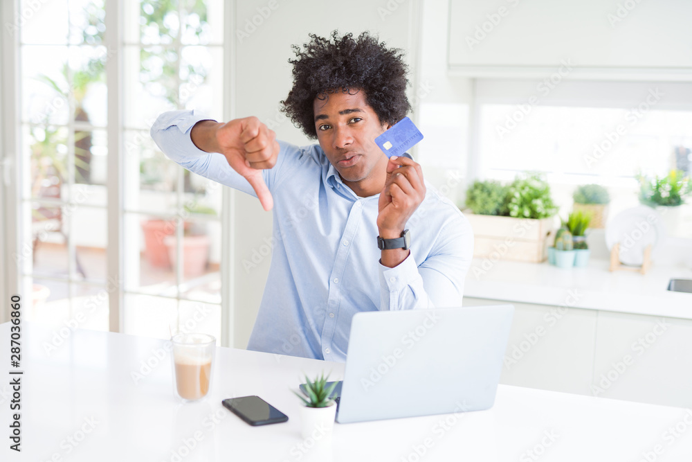 African American man using laptop and shopping online with credit card with angry face, negative sign showing dislike with thumbs down, rejection concept