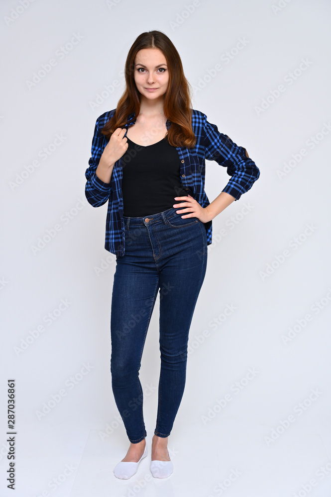 Full-length Vertical Portrait of a cute brunette girl, a young woman with beautiful curly hair in a blue shirt and jeans on a white background. Smiling, talking with emotions, showing hands. Full-length Vertical Portrait of a cute brunette girl, a young woman with beautiful curly hair in a blue shirt and jeans on a white background. Smiling, talking with emotions, showing hands.