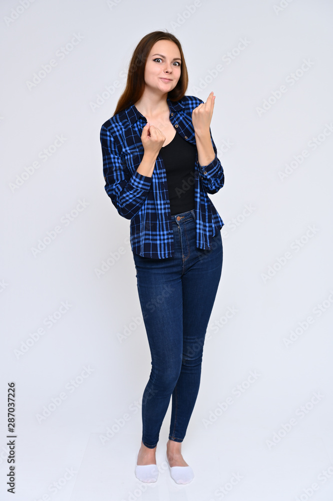 Full-length Vertical Portrait of a cute brunette girl, a young woman with beautiful curly hair in a blue shirt and jeans on a white background. Smiling, talking with emotions, showing hands. Full-length Vertical Portrait of a cute brunette girl, a young woman with beautiful curly hair in a blue shirt and jeans on a white background. Smiling, talking with emotions, showing hands.