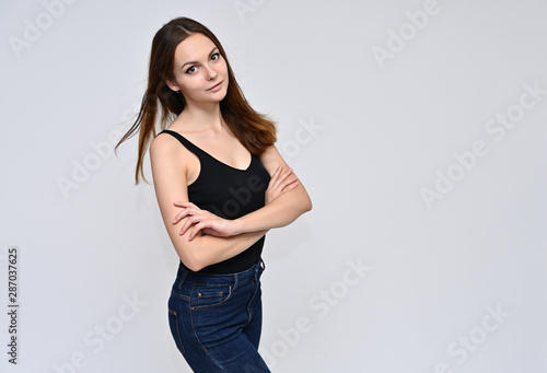 Portrait of a cute brunette girl, a young woman with beautiful curly hair in a black T-shirt on a white background. Smiling, talking with emotions, showing hands to the sides. © Вячеслав Чичаев