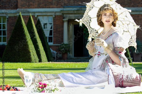 Foto Beautiful lady in regency clothing sitting on lawn in front of stately home hold