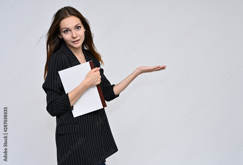 Portrait of a cute brunette girl, a young woman with beautiful curly hair in a black jacket with a folder in her hands on a white background. Smiling, talking with emotions, showing hands. Portrait of a cute brunette girl, a young woman with beautiful curly hair in a black jacket with a folder in her hands on a white background. Smiling, talking with emotions, showing hands.