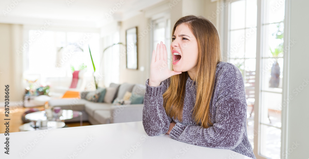 Beautiful young woman at home shouting and screaming loud to side with hand on mouth. Communication concept. Beautiful young woman at home shouting and screaming loud to side with hand on mouth. Communication concept.