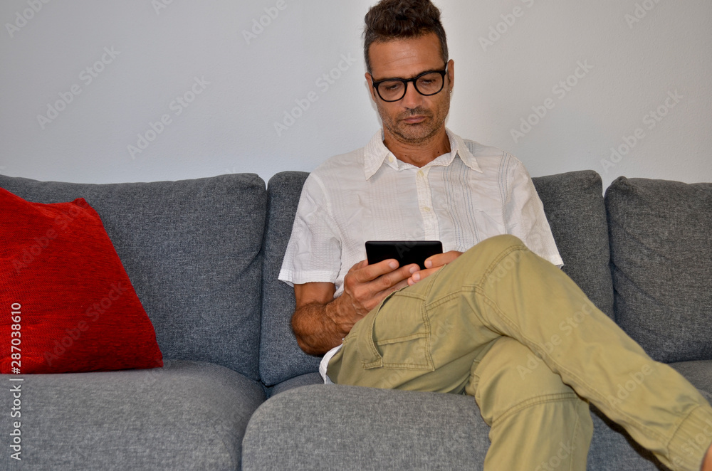 Man with white shirt sitting on a gray sofa reading an electronic book Man with white shirt sitting on a gray sofa reading an electronic book