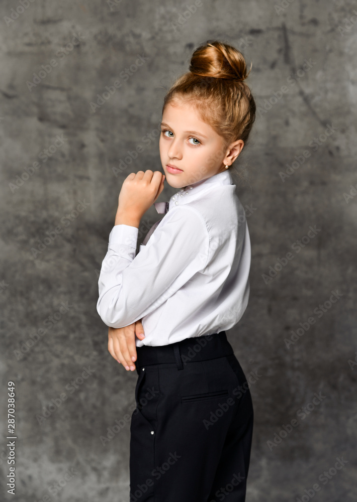 Little female caucasian model posing in school uniform on a gray concrete studio background. Little female caucasian model posing in school uniform on a gray concrete studio background.