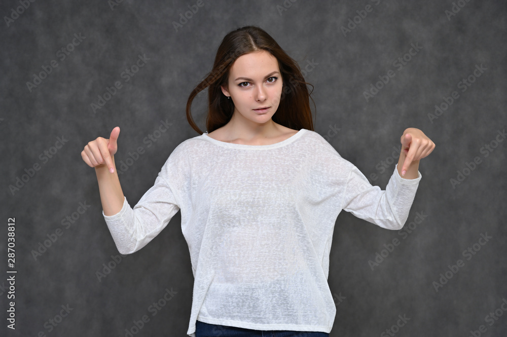 Portrait of a cute brunette girl, a young woman with beautiful curly hair in a white sweater on a gray background. Smiling, talking with emotions, showing hands to the sides. Portrait of a cute brunette girl, a young woman with beautiful curly hair in a white sweater on a gray background. Smiling, talking with emotions, showing hands to the sides.