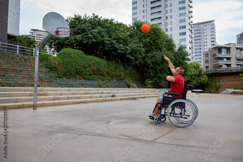 Cripple man in wheelchair plays basketball on open air ground