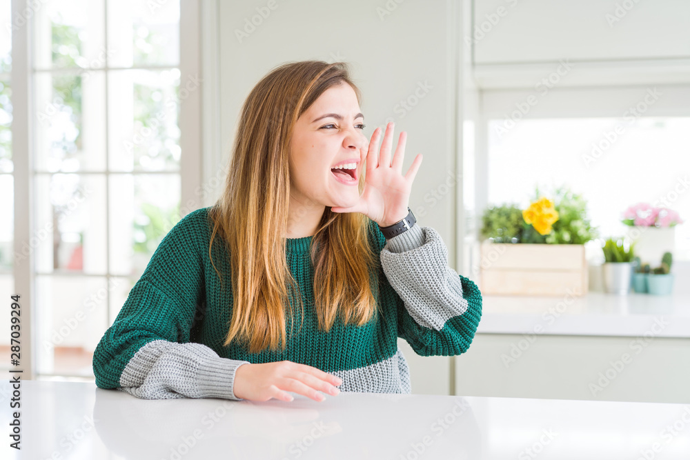 Young beautiful plus size woman wearing casual striped sweater shouting and screaming loud to side with hand on mouth. Communication concept. Young beautiful plus size woman wearing casual striped sweater shouting and screaming loud to side with hand on mouth. Communication concept.