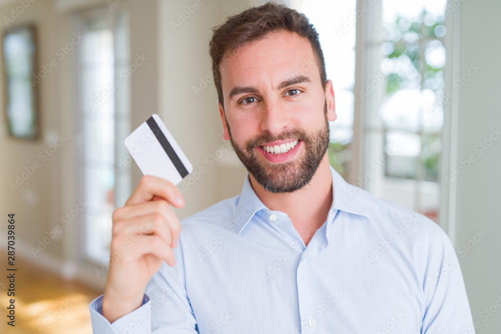 Handsome business man holding credit card with a happy face standing and smiling with a confident smile showing teeth Handsome business man holding credit card with a happy face standing and smiling with a confident smile showing teeth