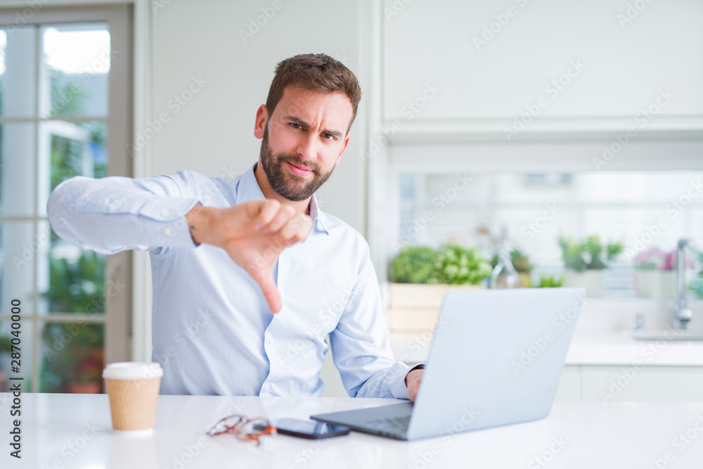 Handsome man working using computer laptop and drinking a cup of coffee with angry face, negative sign showing dislike with thumbs down, rejection concept