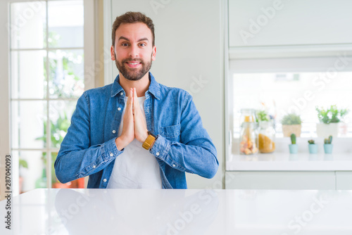 Handsome man at home praying with hands together asking for forgiveness smiling confident. © Krakenimages.com