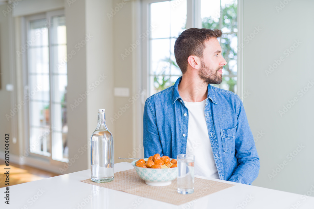 Handsome man eating pasta with meatballs and tomato sauce at home looking to side, relax profile pose with natural face with confident smile.