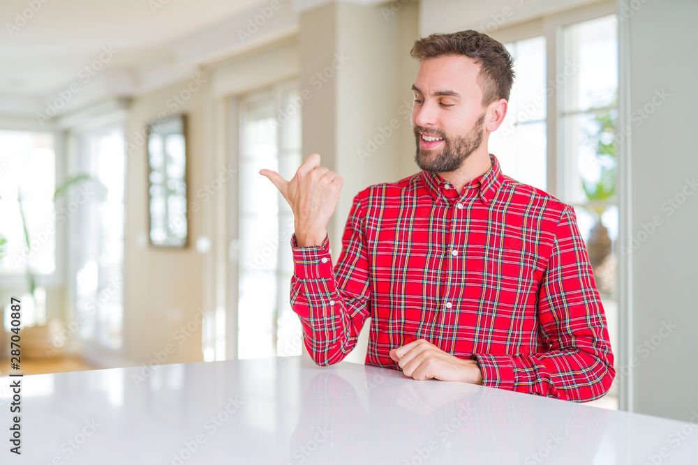 Handsome man wearing colorful shirt smiling with happy face looking and pointing to the side with thumb up. Handsome man wearing colorful shirt smiling with happy face looking and pointing to the side with thumb up.