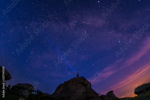 Man on top of a mountain against the background of space, starry sky, the Milky Way. Shining a lantern in the sky