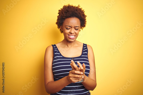 Beauitul african american woman wearing summer t-shirt over isolated yellow background Suffering pain on hands and fingers, arthritis inflammation photo
