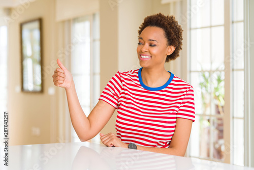 Young beautiful african american woman at home Looking proud  smiling doing thumbs up gesture to the side
