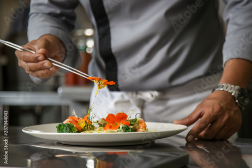 Fototapeta Naklejka Na Ścianę i Meble -  Closeup of male chef arranging edible flowers on the meal in the commercial kitchen