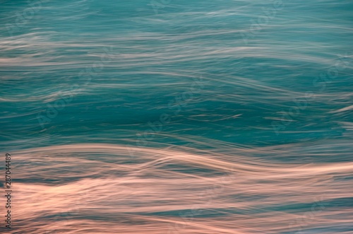 Abstract dynamic, dark turquoise and glowing sunset, background in the form of wavy stripes of lines.